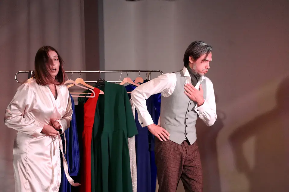 Two singers in a scene beside a clothes rail
