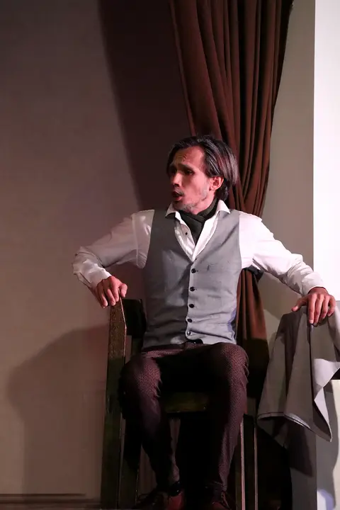 A singer wearing a waistcoat seated on a chair